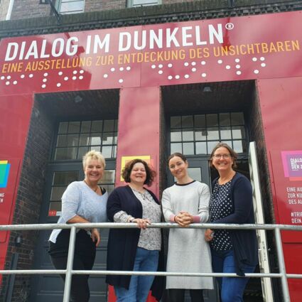 Saskia Timm, Wiebke Messerschmidt, Miriam Hornung und Ilka Pfänder stehen vor dem Eingang der Ausstellung „Dialog im Dunklen“