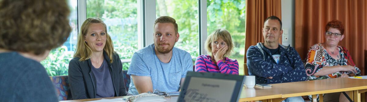 Zwei Männer und drei Frauen sitzen an Tischen und lassen sich beraten