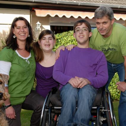 Eltern mit ihrem Sohn im Rollstuhl, ihrer Tochter und einem Hund lächeln in die Kamera