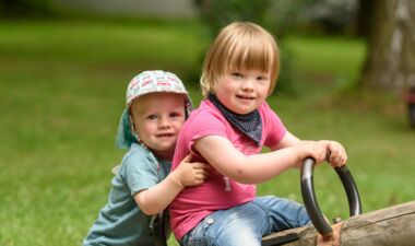 Zwei kleine Kinder sitzen gemeinsam auf einer Holzwippe