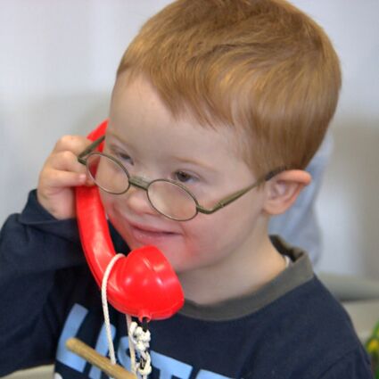 Ein behinderter Junge hält sich fröhlich einen roten Telefonhörer ans Ohr