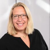 Eine Frau mit schulterlangen, blonden Haaren und Brille lacht in die Kamera