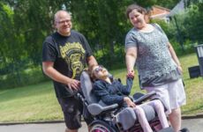 Zwei Eltern gehen mit ihrem behinderten Kind in einem Rollstuhl spazieren