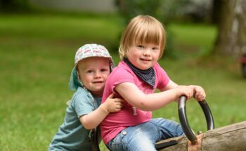 Zwei kleine Kinder sitzen gemeinsam auf einer Holzwippe