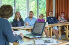Zwei Männer und drei Frauen sitzen an Tischen und lassen sich schulen
